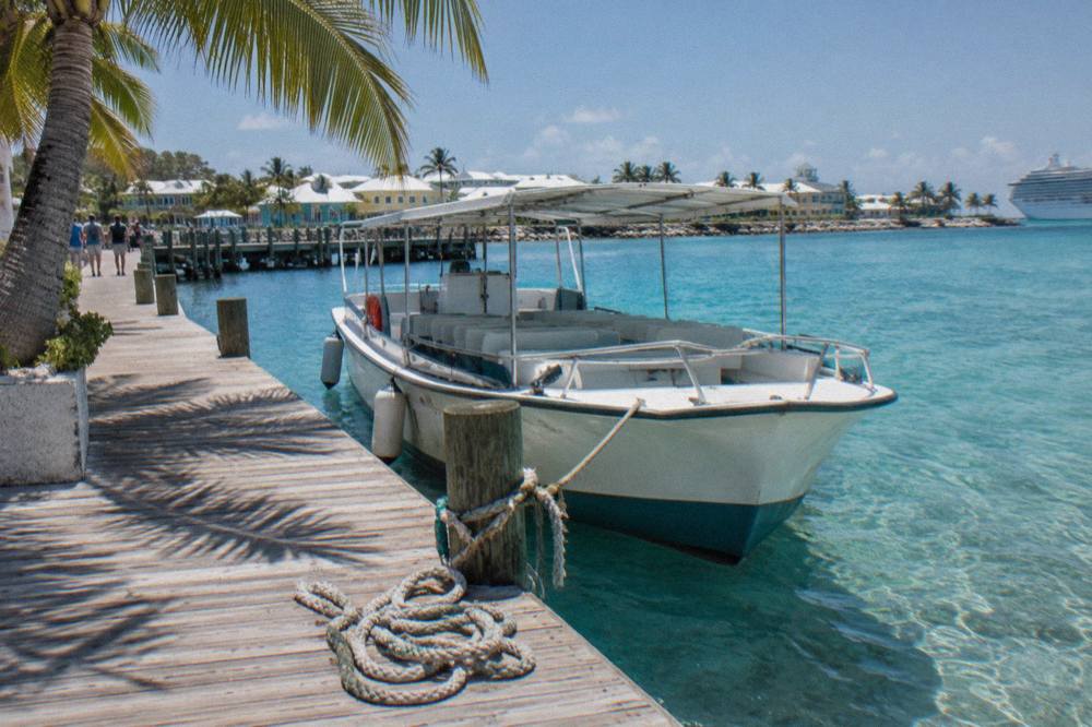 A tour boat tied at a wooden dock in clear shallow water near Nassau