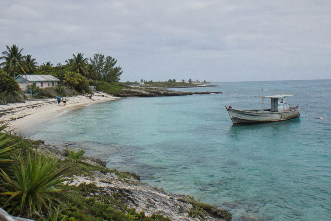 Turquoise shallow water along a small Bahamian island shoreline with a wooden boat anchored offshore