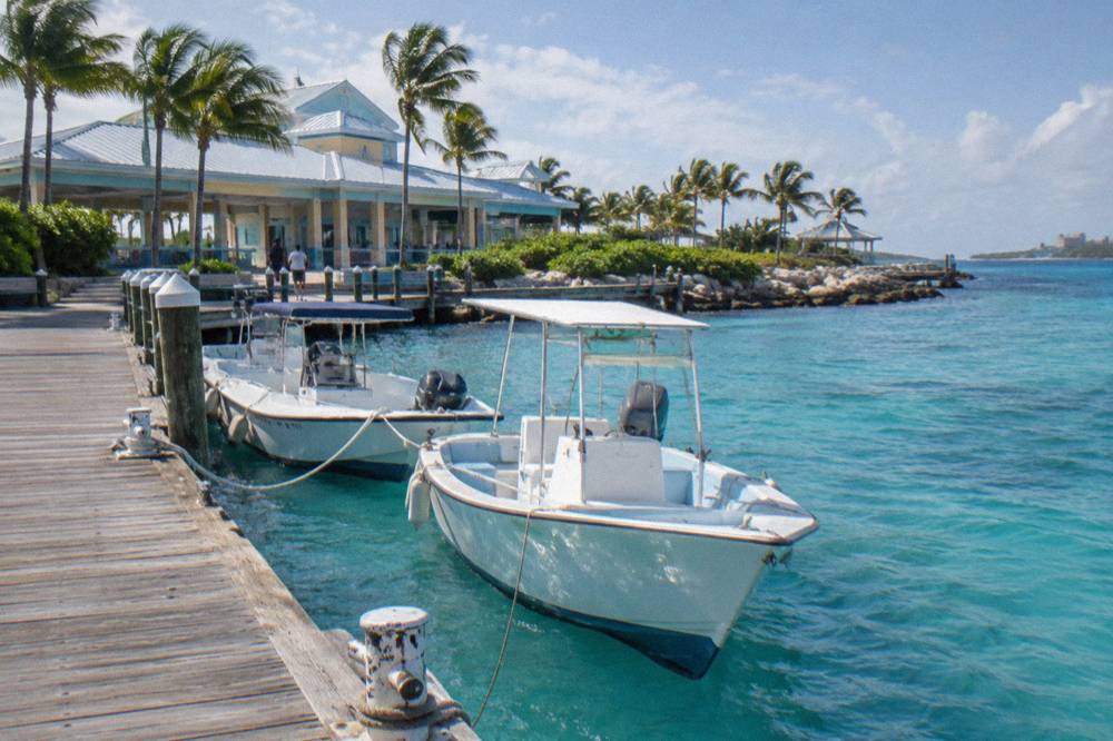 Small powerboats tied along a wooden dock beside turquoise shallows