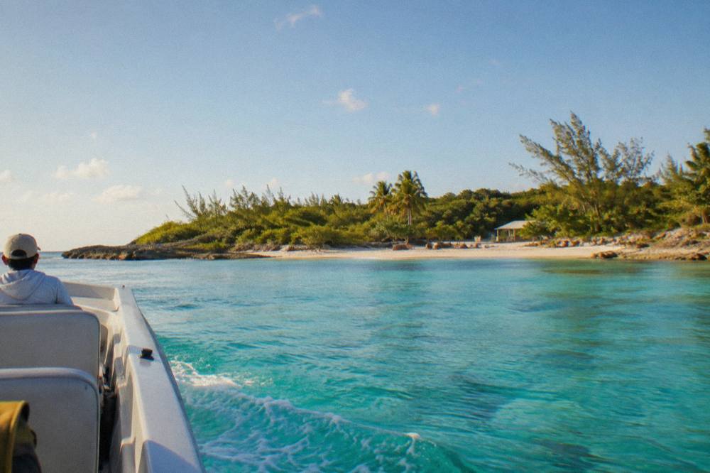 A small passenger boat crossing calm turquoise water toward a green island shoreline