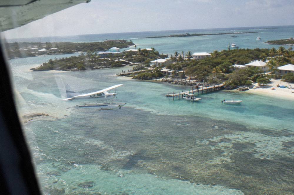 A light aircraft flying low over small green cays and shallow turquoise water