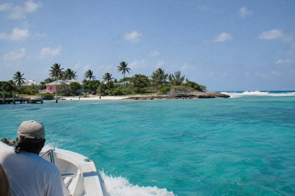 Small boat crossing clear turquoise water toward a green Bahamian island