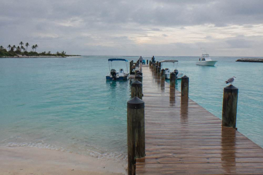 Wooden dock extending into calm turquoise water with boats moored nearby