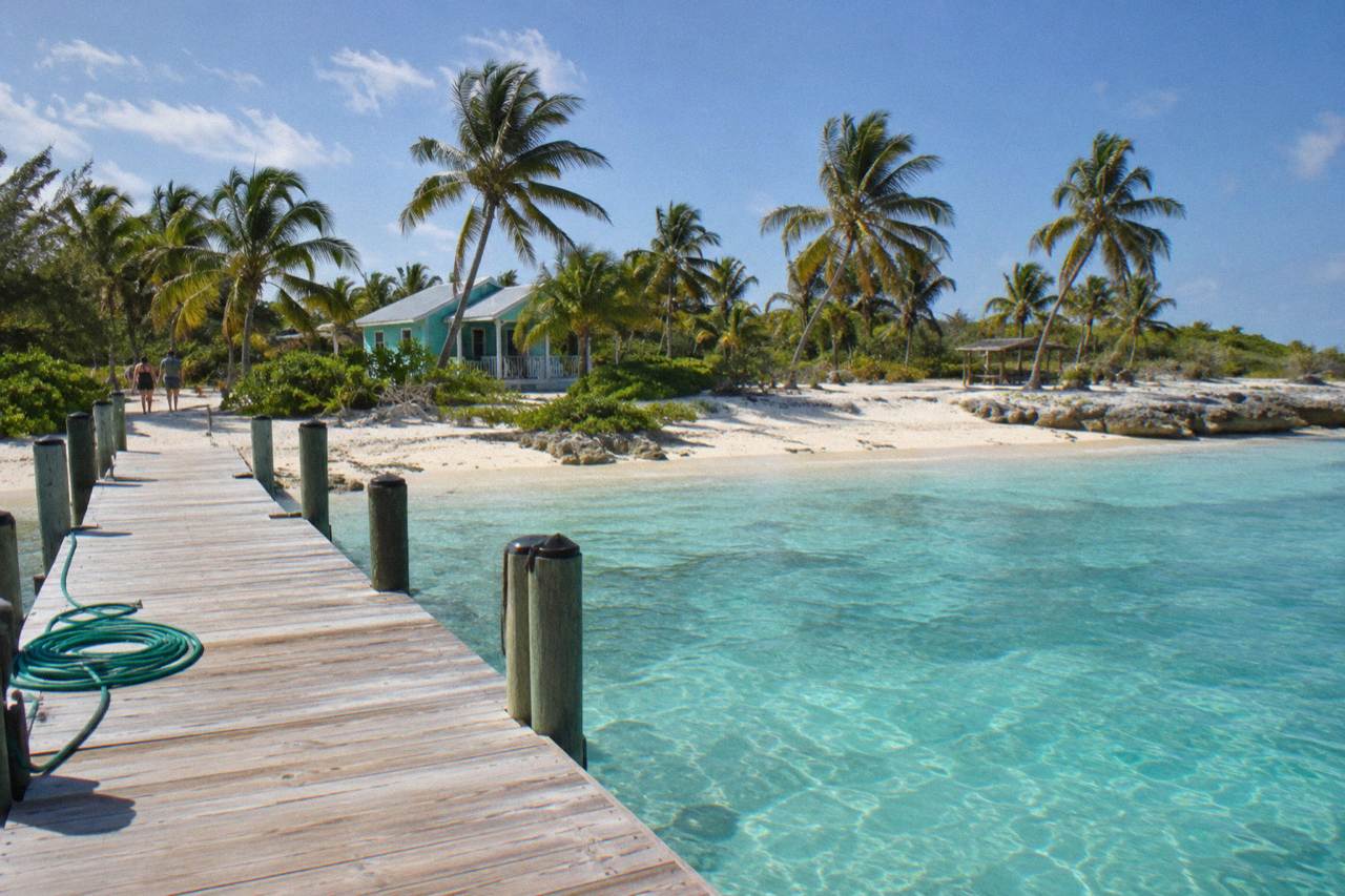 A small island beach with turquoise shallows and a wooden dock under a clear sky