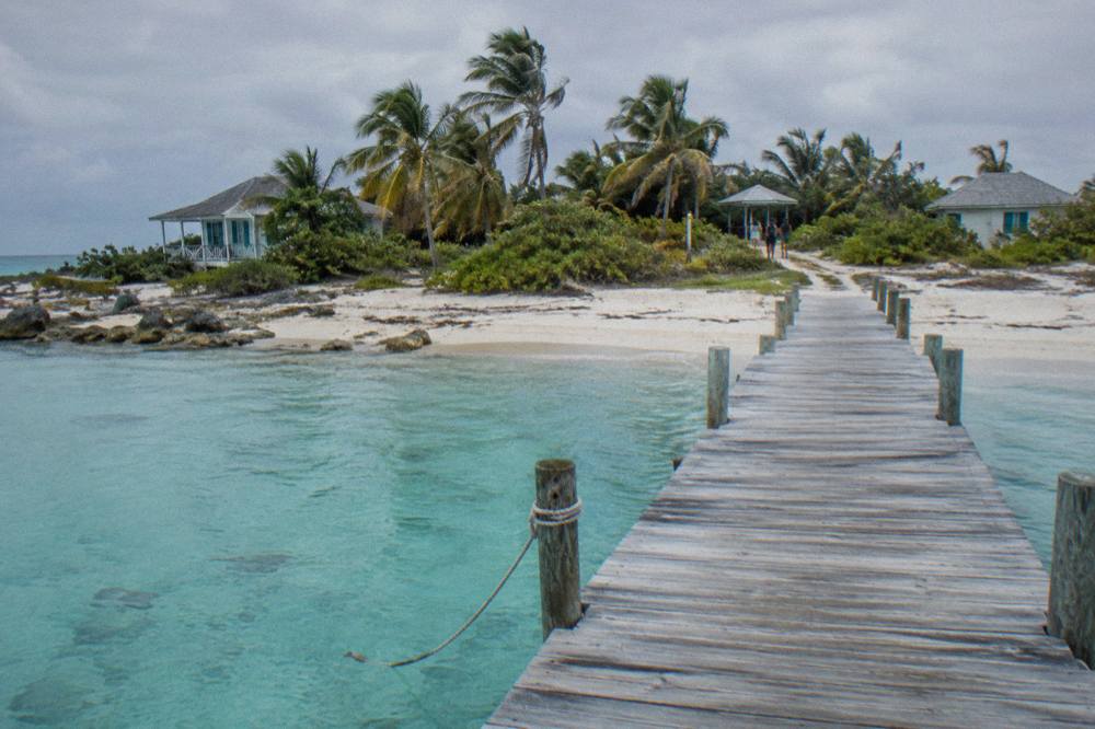 A white sand beach with calm shallow water and a wooden dock extending into the sea