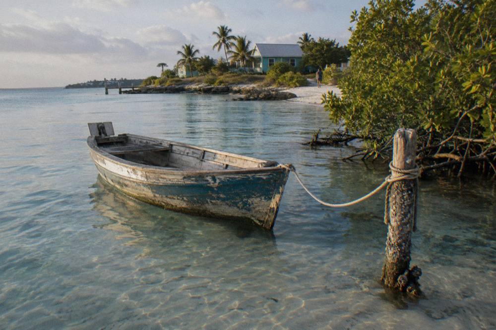 A wooden boat moored in clear shallow water beside a green island shoreline.