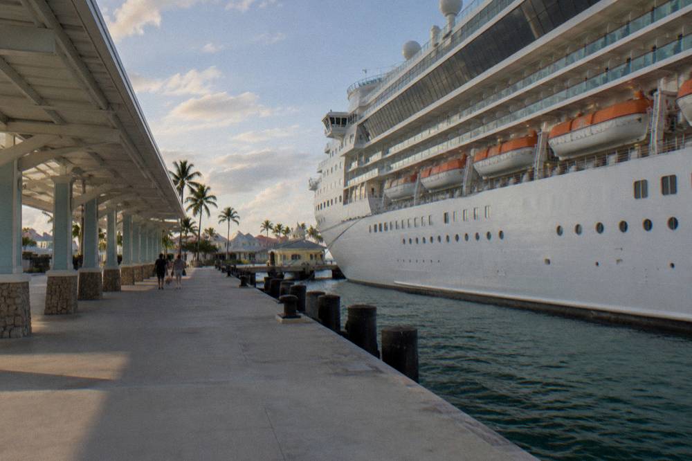A large cruise ship docked at a pier beside a waterfront terminal building.