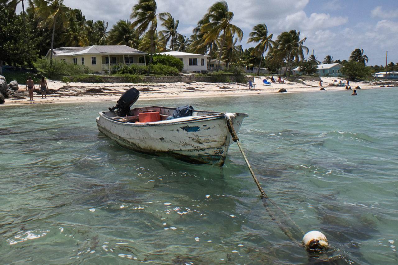 Turquoise water and a small boat anchored off a sandy beach with palm trees.