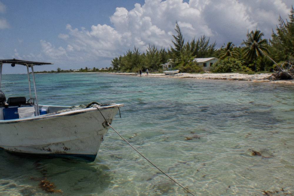 A boat anchored in shallow clear water beside a small green island under a wide sky