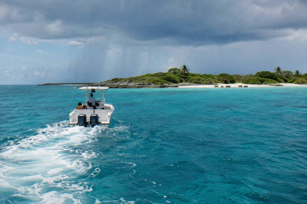 A powerboat crossing open turquoise water toward low green islands