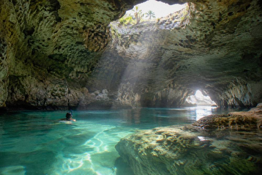 A flooded cave interior with shafts of sunlight through openings above clear water
