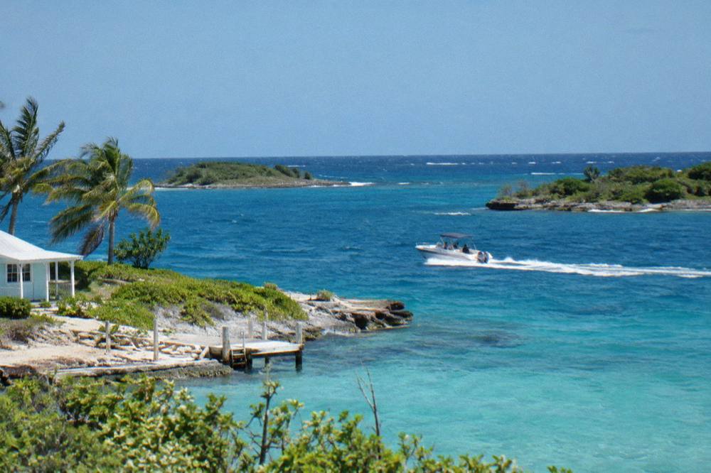 A speedboat crossing open blue water between small cays under a clear sky
