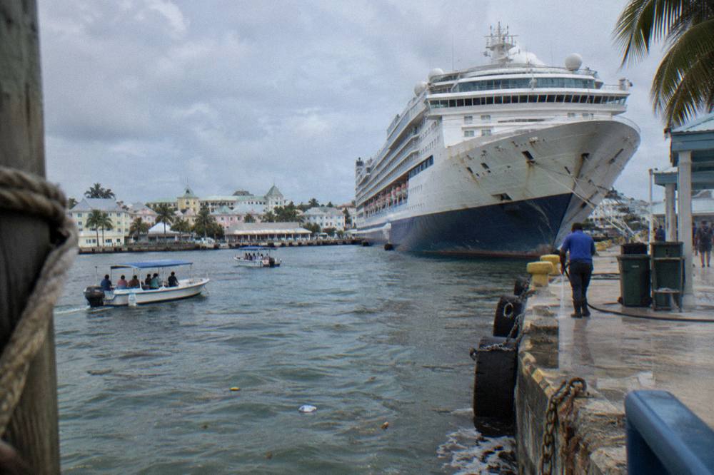 A cruise ship docked at a waterfront terminal with tour boats in the foreground