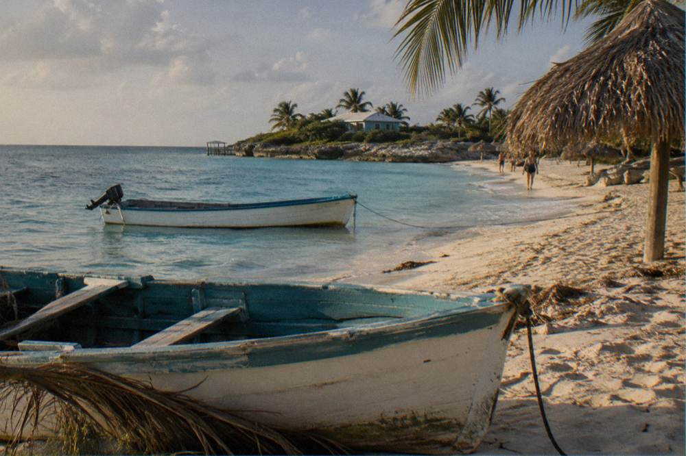 Wooden boats moored beside a white sand beach with palm thatch shade umbrellas