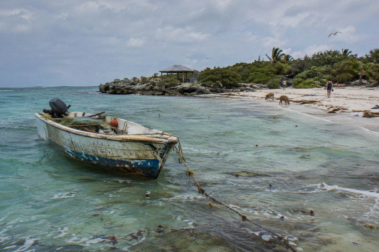 Turquoise shallow water around a small Bahamian island with a wooden boat anchored offshore