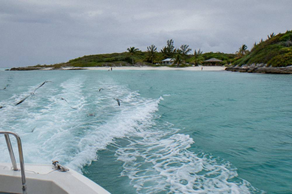 Boat wake crossing bright turquoise water toward a small green island