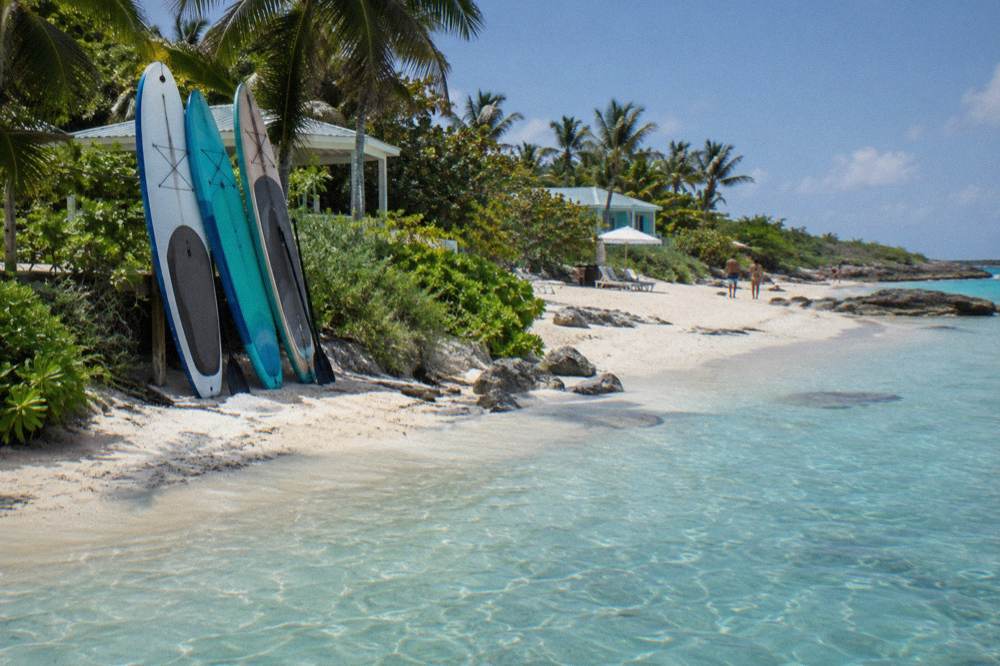 A calm swimming beach with paddle boards resting on white sand and clear shallow water