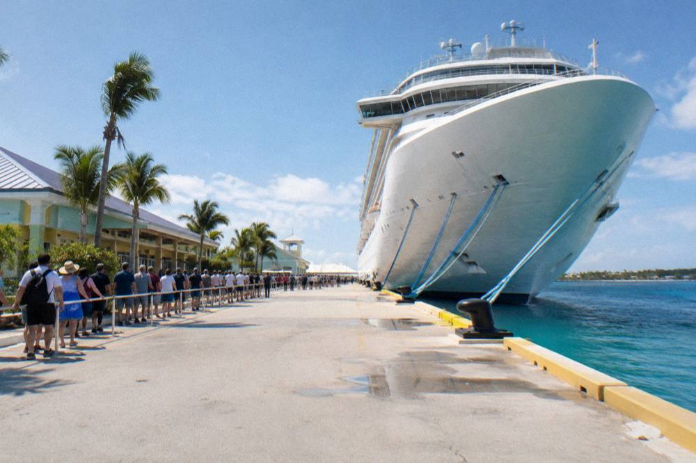 A cruise ship docked at a busy port terminal with passengers walking along the pier