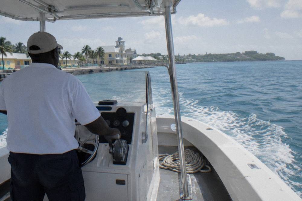 A small boat with a captain standing at the helm steering toward a green island