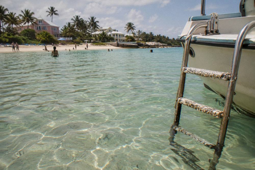 Shallow clear water over pale sand with a swim ladder hanging from a small boat