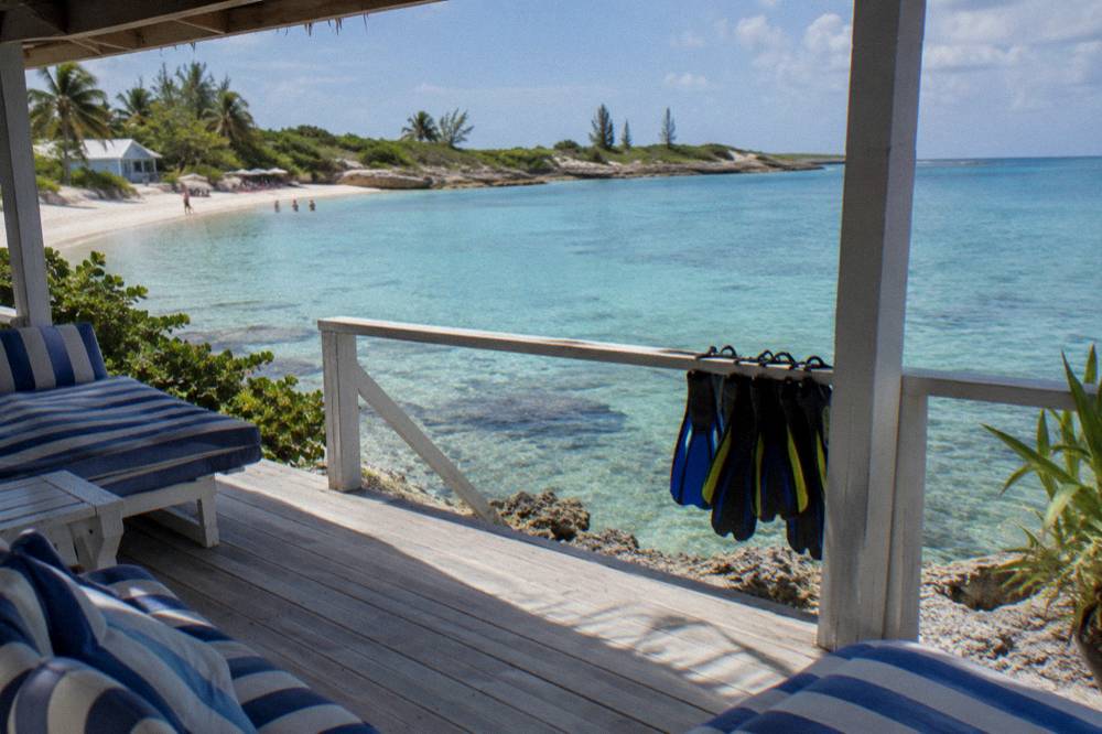 Beach chairs and a shaded lounging area on sand beside calm clear water
