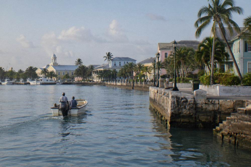A small boat crossing calm turquoise harbor water toward a wooded island