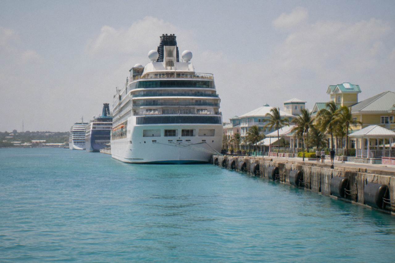 Cruise ships docked along a waterfront pier with turquoise harbor water in the foreground