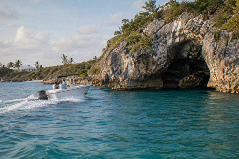 An open speedboat cutting across calm turquoise water toward low green cays