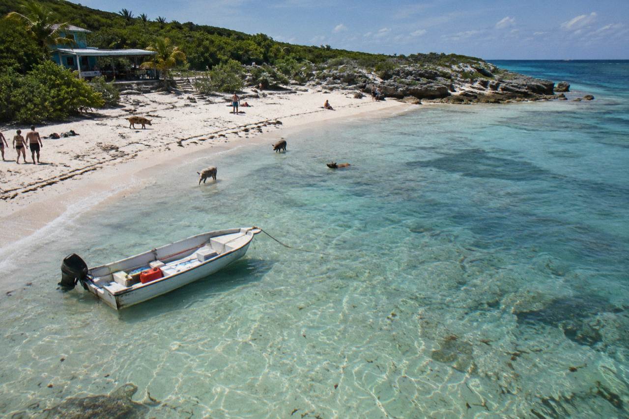 A turquoise Exuma sandbar with calm shallow water and a small boat anchored offshore