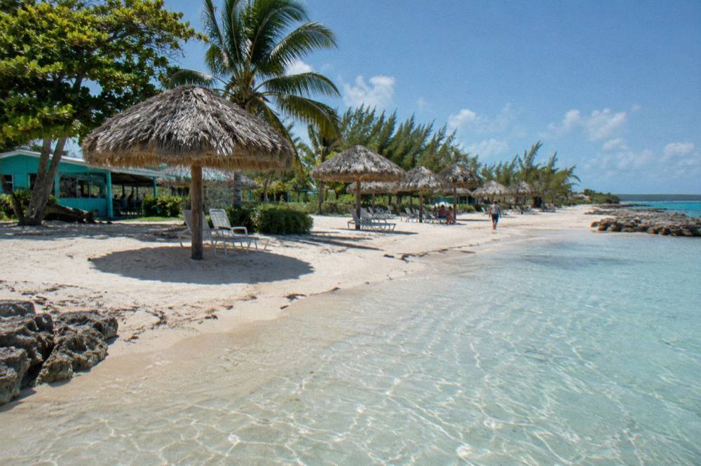 Clear shallow water over pale sand at a beach with thatched shade umbrellas