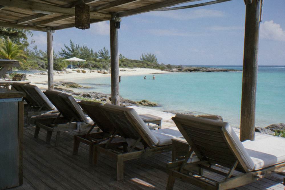 A shaded beach deck with empty lounge chairs facing calm blue water