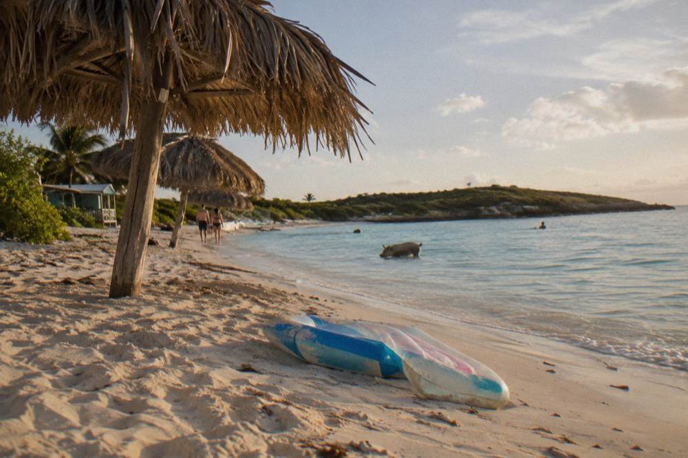 A small island beach with thatched shade umbrellas and clear shallow water