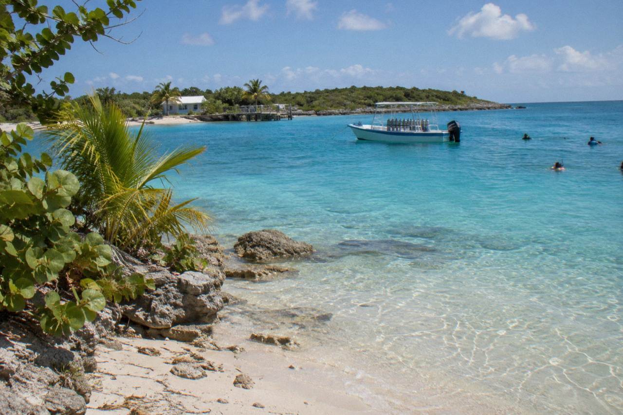 Turquoise water and a sandy beach on a small Bahamian island with a small boat anchored offshore