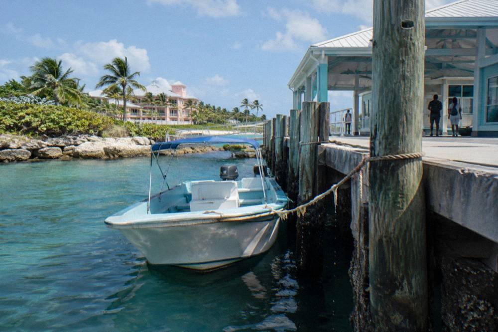 A small boat tied at a wooden dock beside clear green water and low coastal vegetation