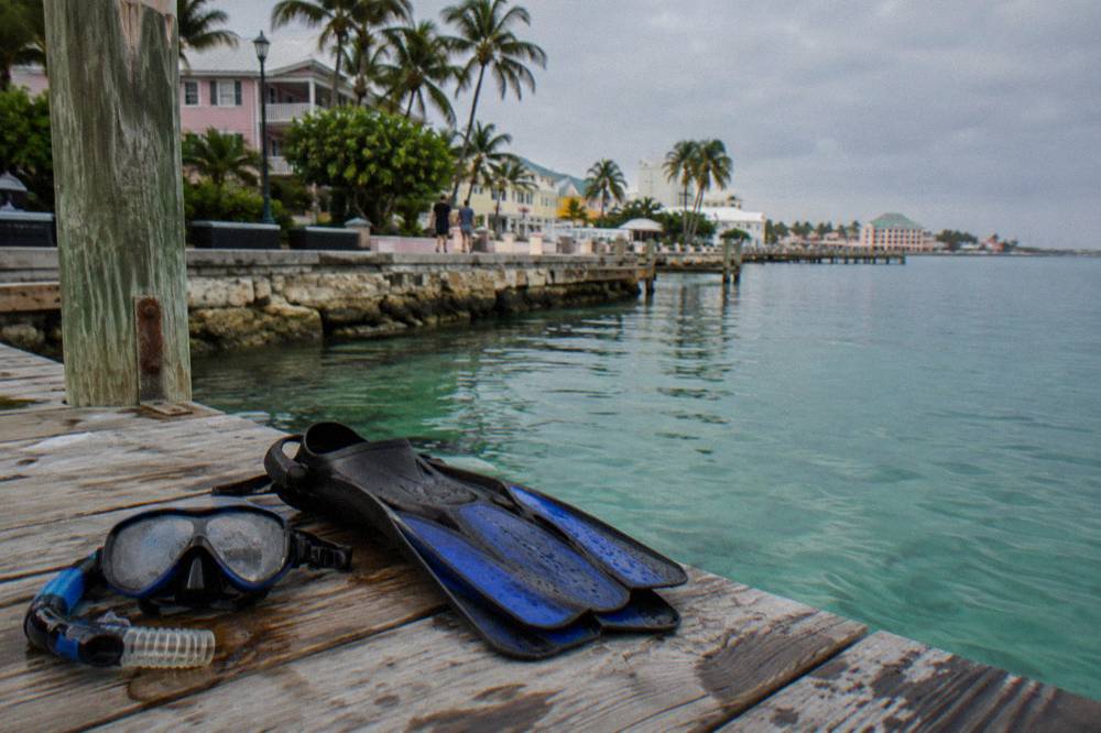 A snorkel mask and fins resting on a wooden dock beside calm water