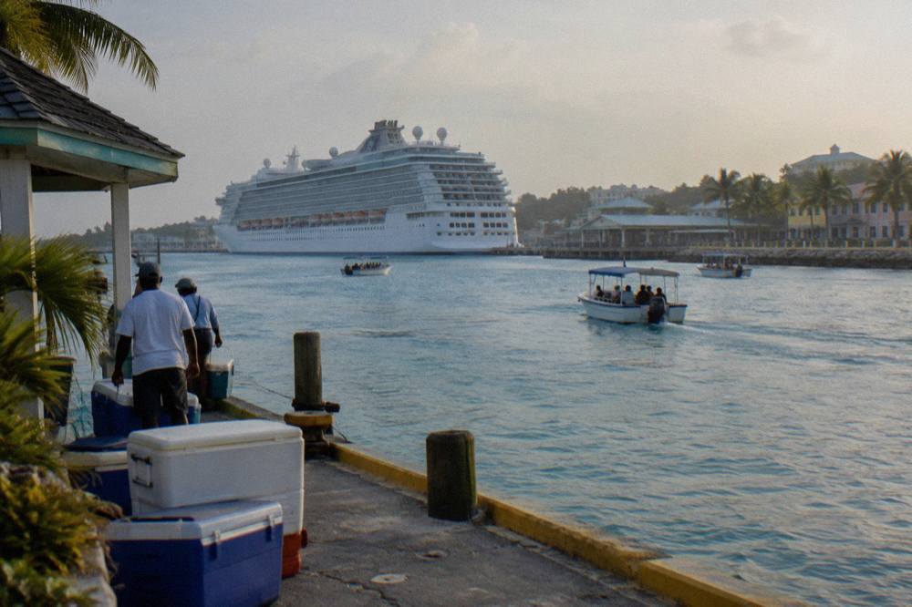 A cruise ship at berth seen across a harbor with tour boats heading out to sea