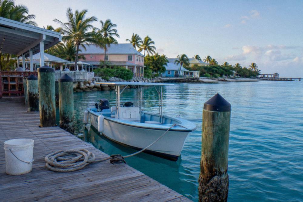 A wooden jetty in a harbor with a small tour boat tied up and pastel buildings along the shore