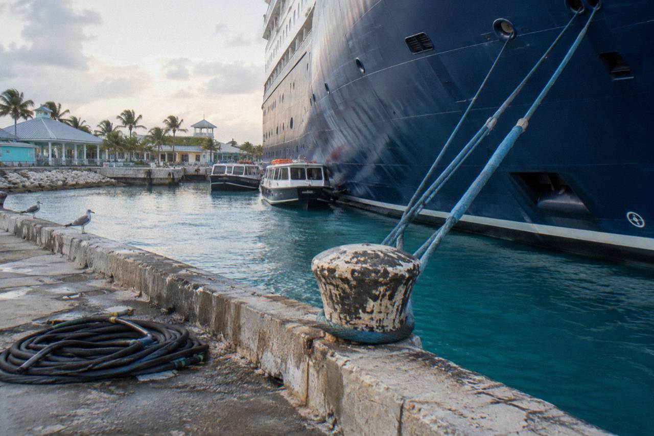A cruise ship docked at a waterfront port terminal with small boats moored nearby