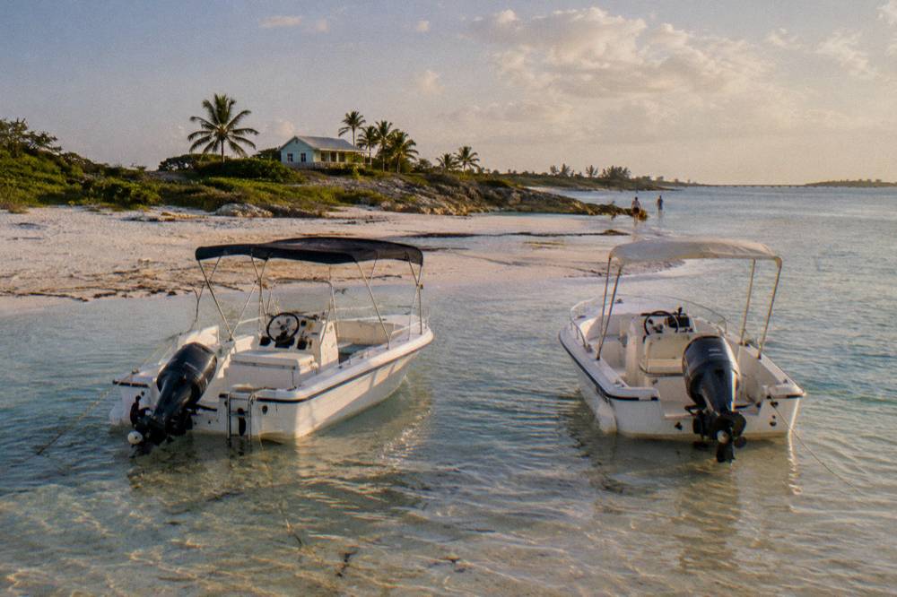 Two small speedboats anchored side by side in shallow water near a sandbar