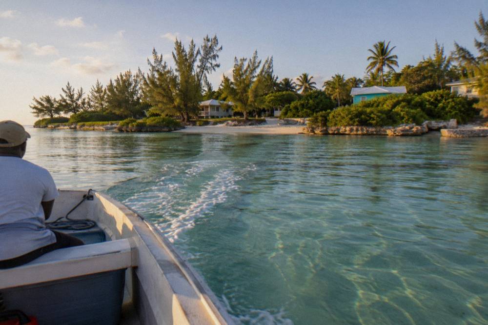 A small boat crossing clear shallow water toward a green island