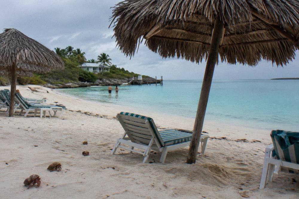 A calm beach with thatched shade umbrellas, lounge chairs and still turquoise water