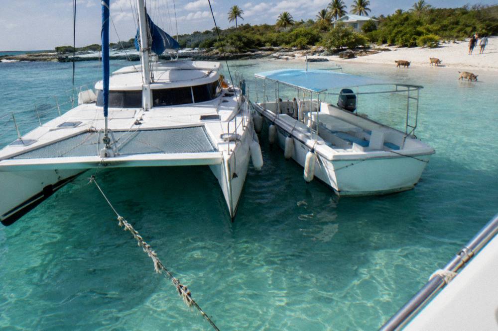 A catamaran and small boat moored side by side over pale sand visible through clear water