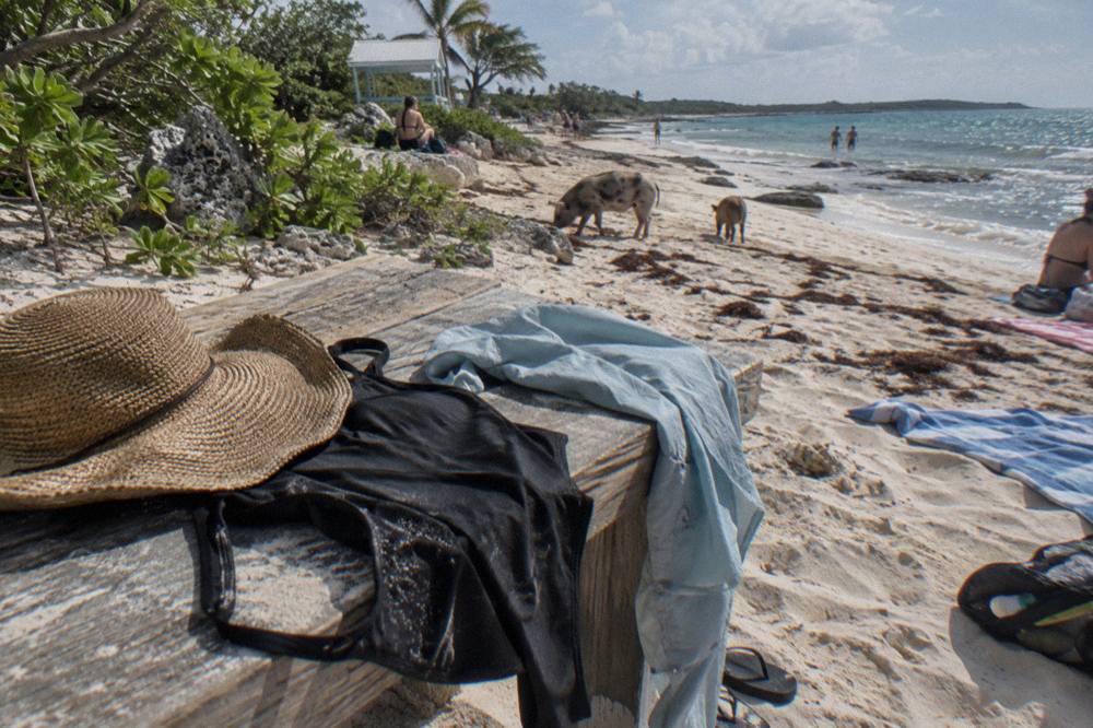 A swimsuit, sun hat and quick-dry shirt laid out on a wooden bench beside a beach towel