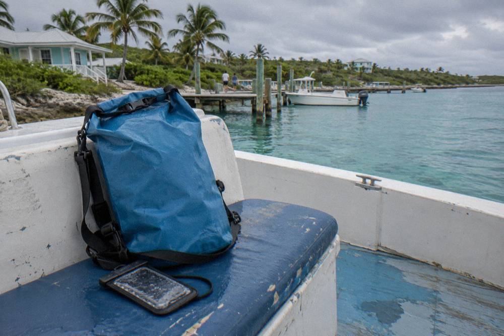 A dry bag and waterproof phone pouch resting on a boat seat beside a bottle of sunscreen