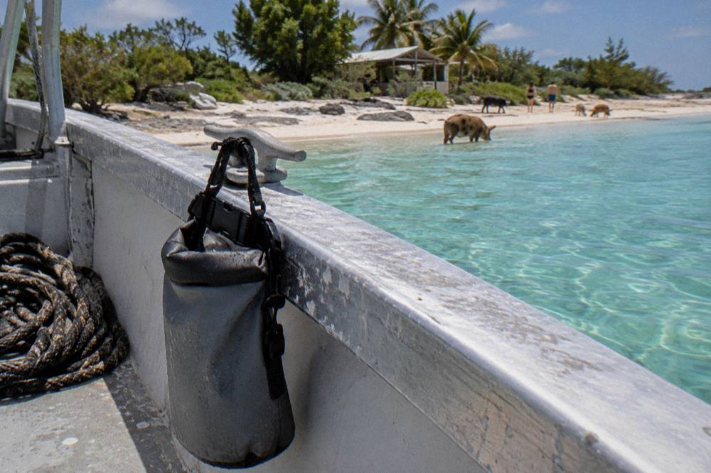 A small dry bag hanging from a boat rail above a turquoise shallow near a beach