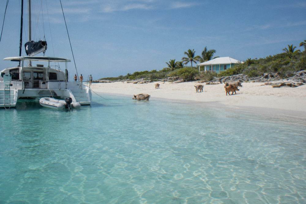 A catamaran anchored beside a sandbar in clear shallow Exuma water